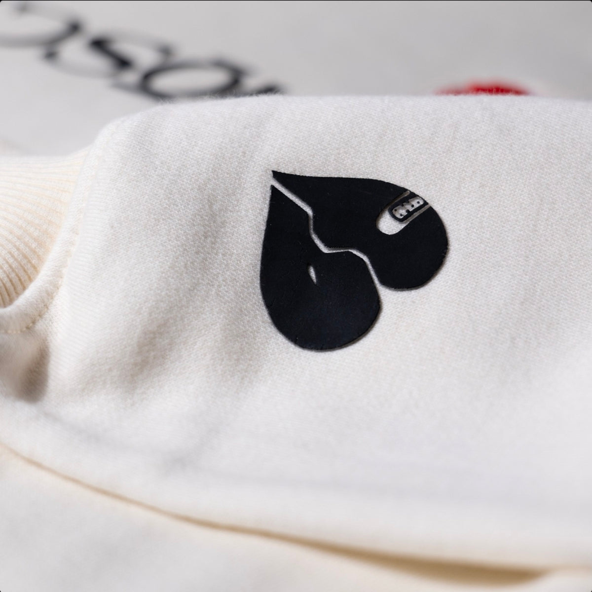 Close-up of the black raised 3D broken-heart sleeve detail on the off-white KiiNDSOULS heavyweight hoodie