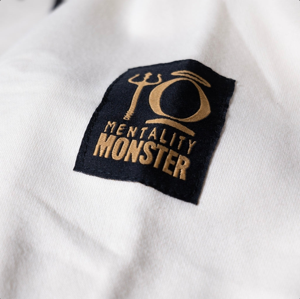 Close-up of the black and gold Mentality Monster embroidered patch on the off-white KiiNDSOULS hoodie