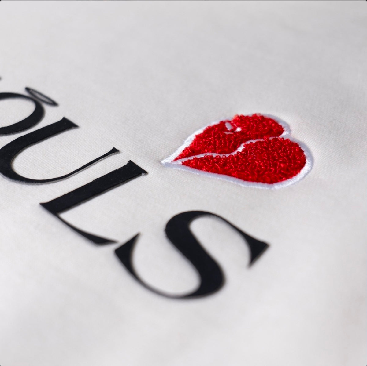 Close-up of red chenille broken-heart embroidery on the off-white KiiNDSOULS heavyweight hoodie